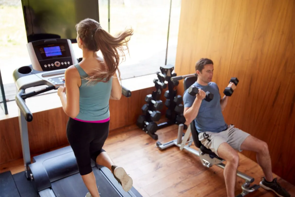 couple in home gym exercising with weights and using running mac