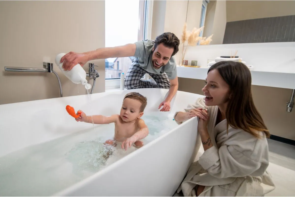 smiling parents looking at baby playing in bathtub