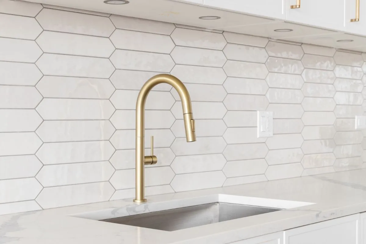 a kitchen detail with white cabinets, gold faucet, and tiled backsplash